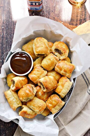 Puff pastry sausage rolls served in a basket with a bowl of dipping sauce.