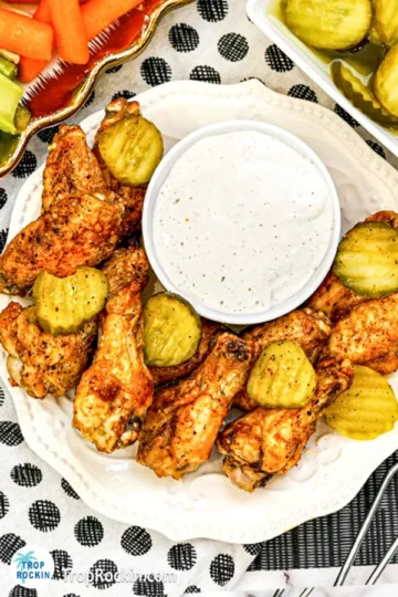 Air fryer chicken wings on a serving plate with pickle slices and dipping sauce.