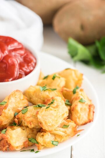 Air fryer tater tots on a serving plate with a bowl of ketchup.
