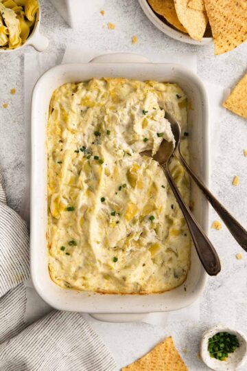Casserole dish filled with artichoke dip and a serving spoon.