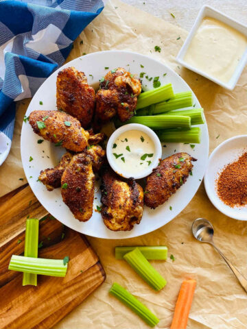 A plate of cajun wings with celery and a dipping sauce.