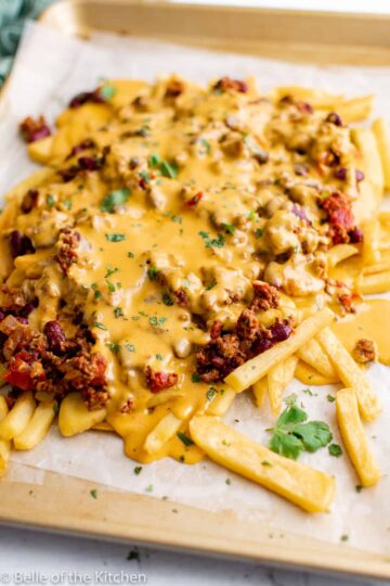Fries on a baking sheet, topped with melted cheese and chili.
