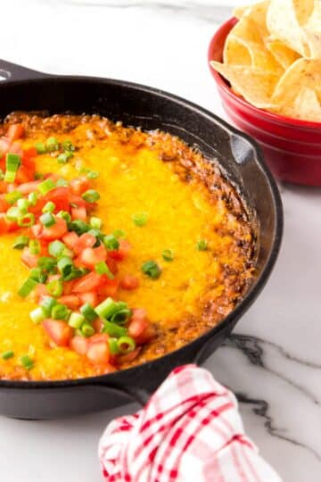 A skillet of chili cheese dip topped with tomatoes and onions.