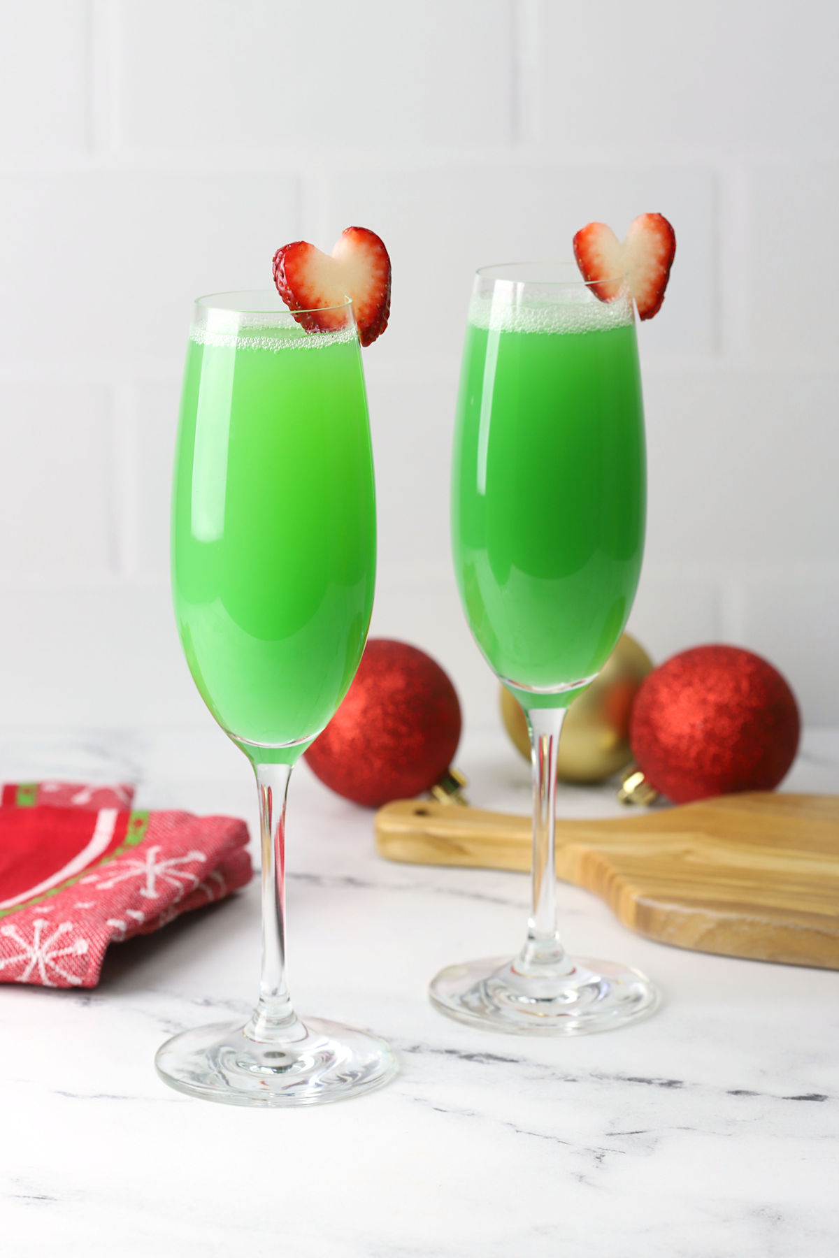 Grinch mimosas on a counter top with strawberry garnishes.