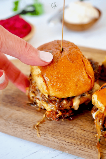A hand grabbing a slider from a wooden serving board.