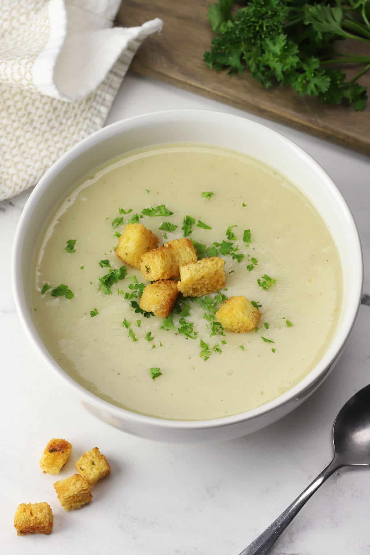 A white bowl filled with Irish potato soup, chopped parsley, and croutons.