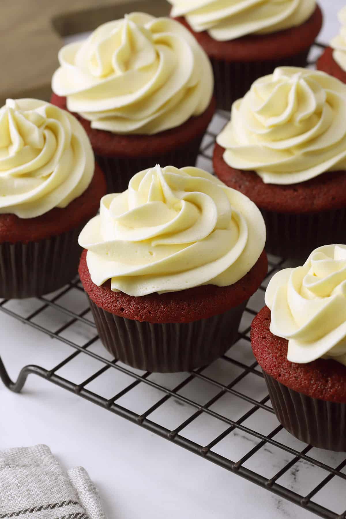 Rows of red velvet cupcakes topped with piped ermine frosting.