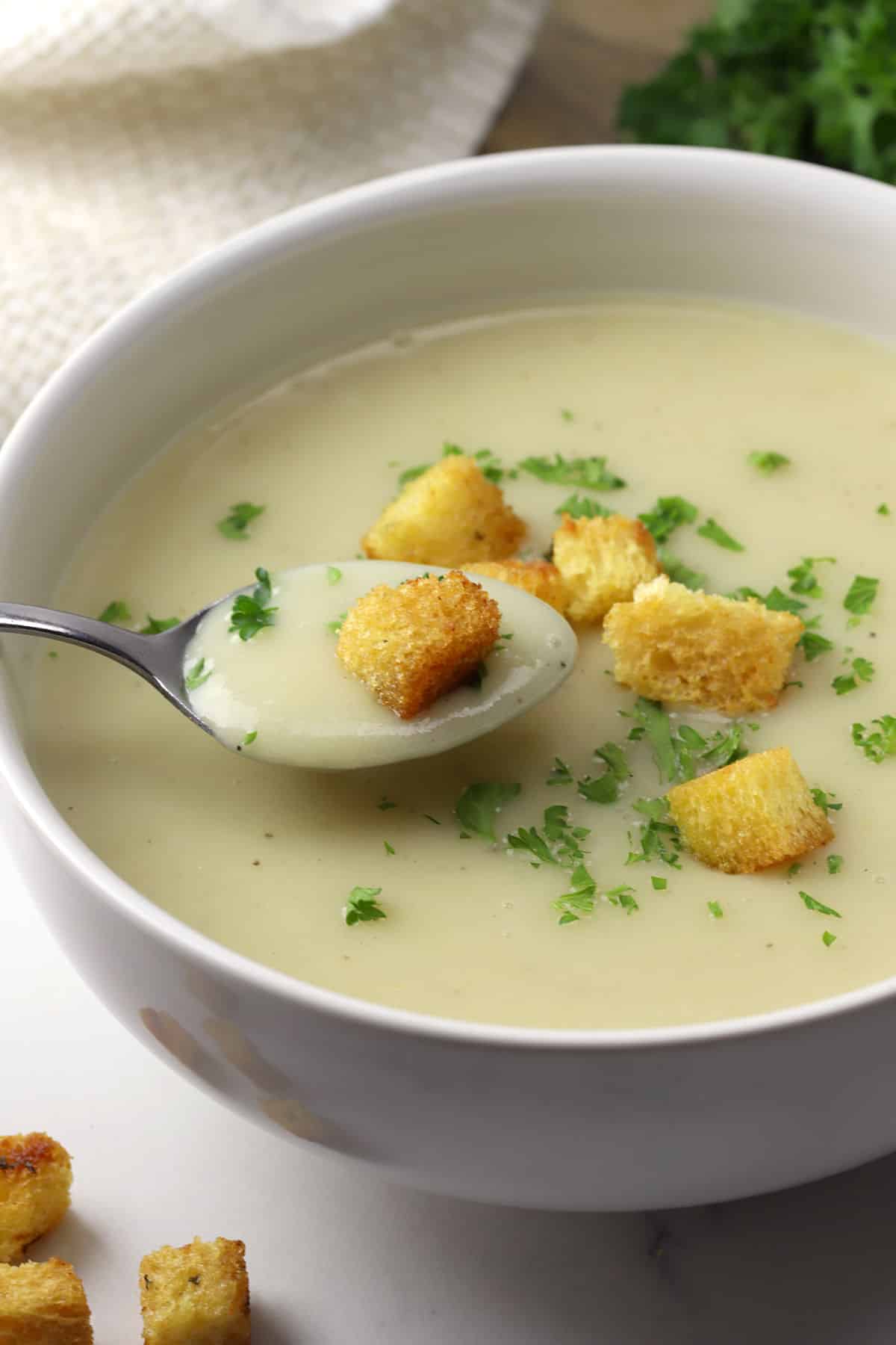 A metal spoon scooping creamy potato soup from a white bowl.