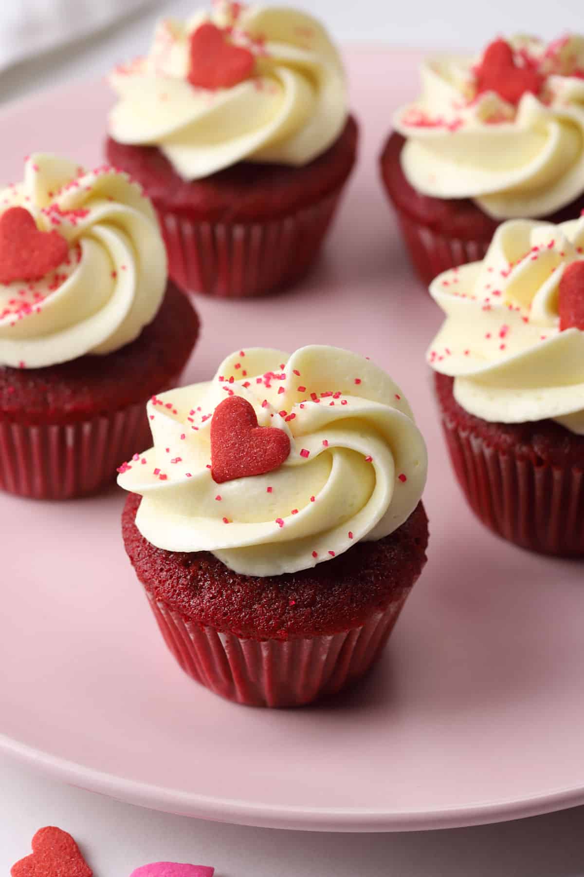 Close up of mini red velvet cupcake topped with a red heart shaped sprinkle.