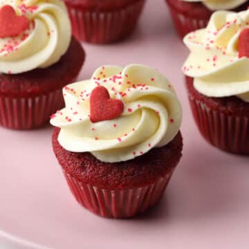 Close up of mini red velvet cupcake topped with a red heart shaped sprinkle.