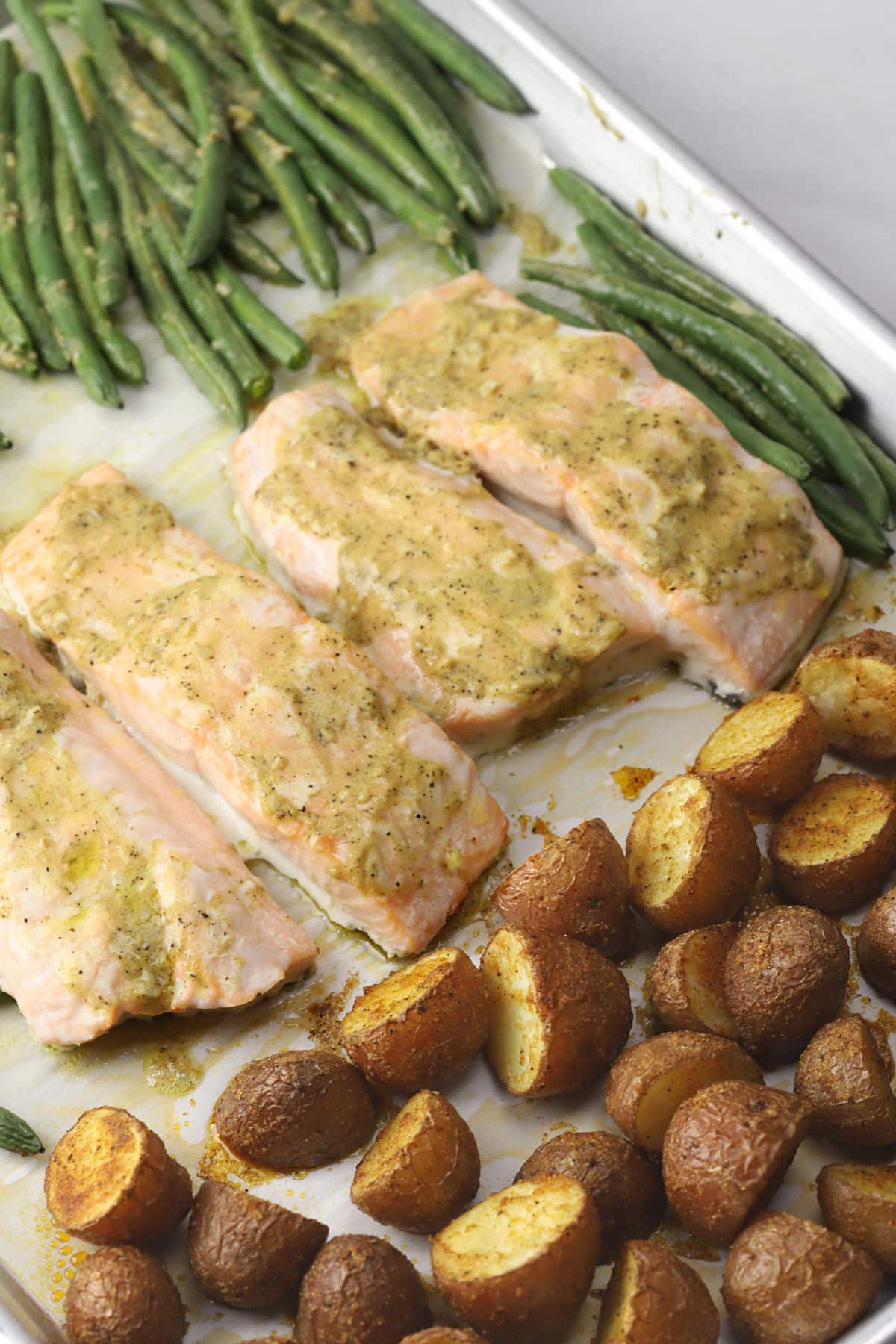 Close up of baked salmon on a sheet pan surrounded by vegetables.