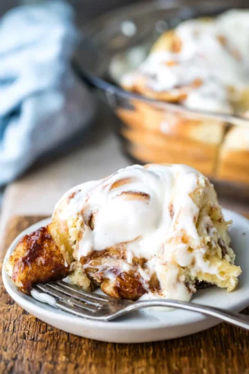 A frosted cinnamon roll on a plate with a fork.