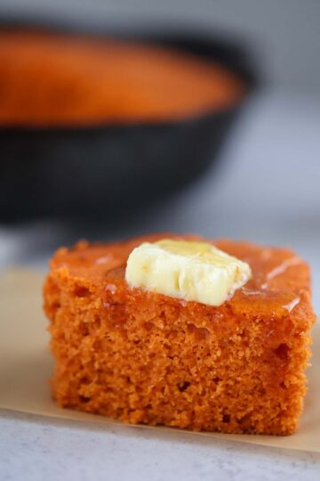 A slice of sweet potato cornbread with a pad of butter melting on top.