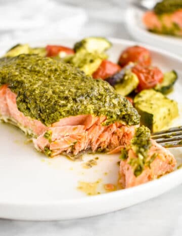 A filet of salmon covered in pesto on a white plate.