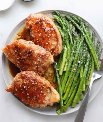 Three pork chops on a white plate with asparagus spears.