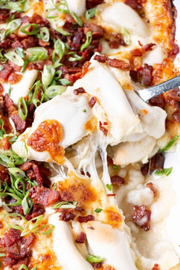 A dish full of pierogi topped with cheese, bacon, and scallions.