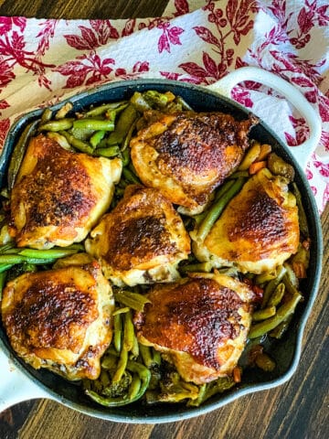 Six chicken thighs on a bed of green beans.