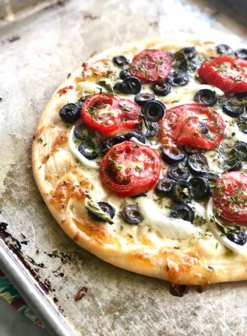 Round flatbread with tomatoes and olives on a baking sheet.