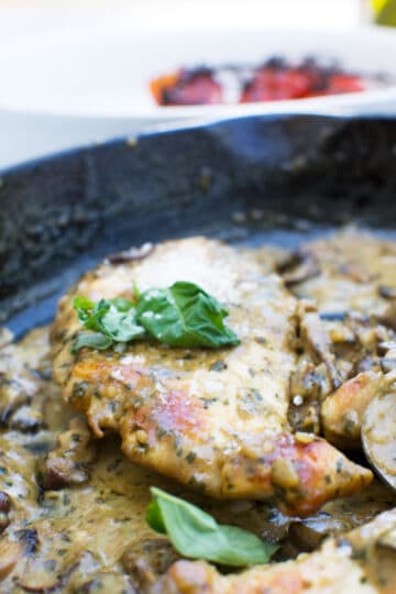 Cooked chicken breast and mushrooms in a cast iron skillet with a creamy sauce.