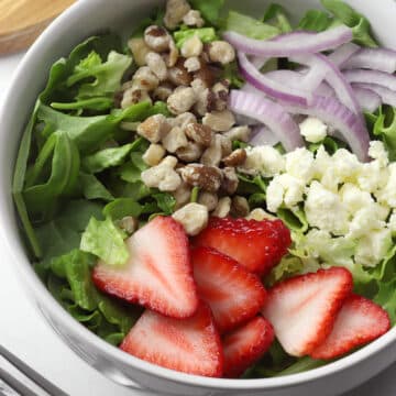 Close up of strawberries, walnuts, feta cheese, and onions on a bed of lettuce.