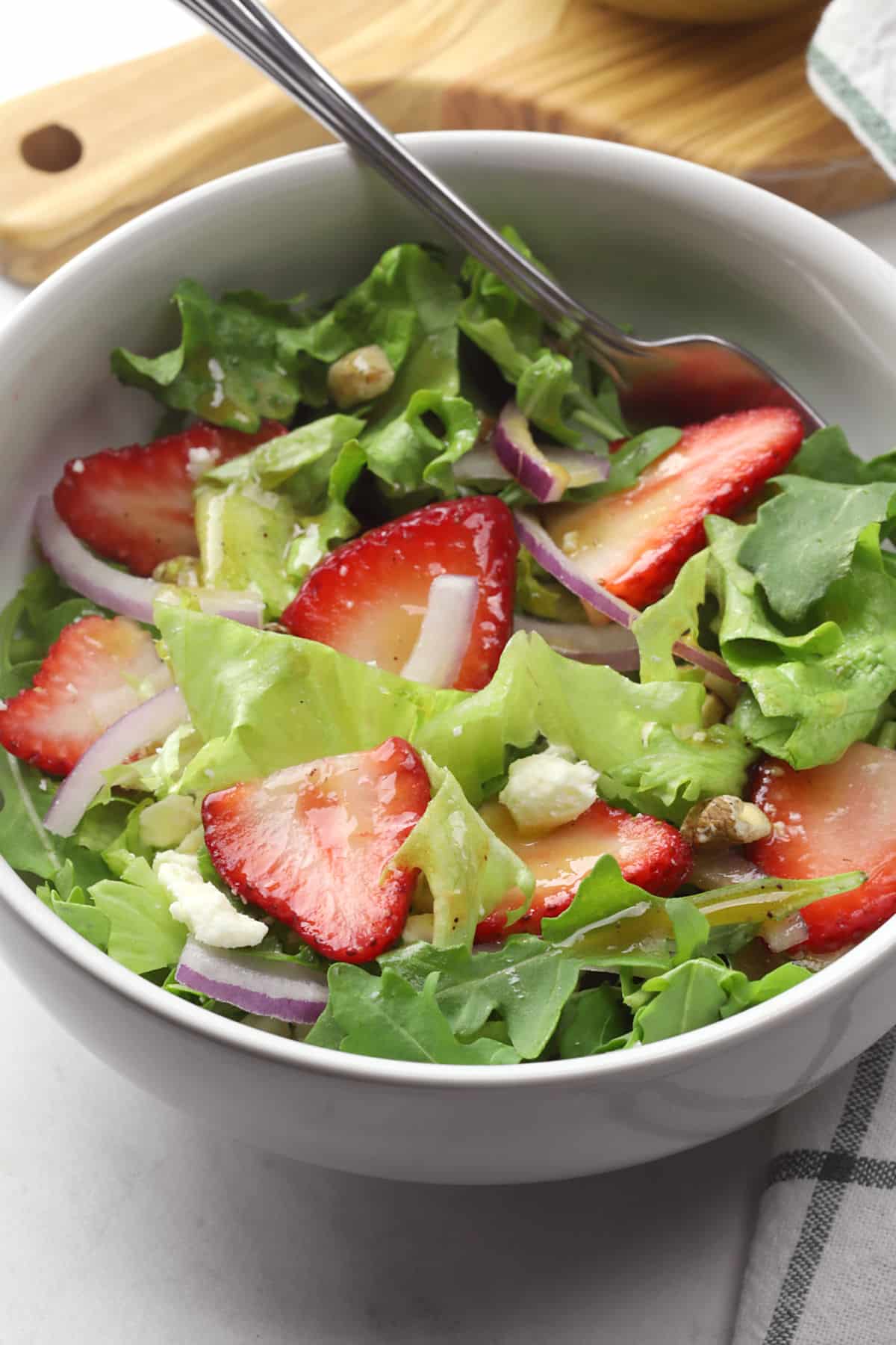 Strawberry walnut salad tossed in a white bowl with a fork.