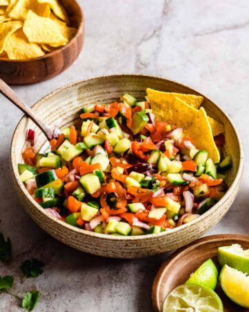 Bowl of cucumber pico de gallo with a wooden serving spoon and tortilla chips.
