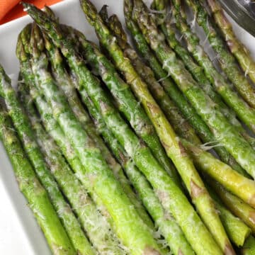 Grilled asparagus topped with melted parmesan cheese on a white serving plate.
