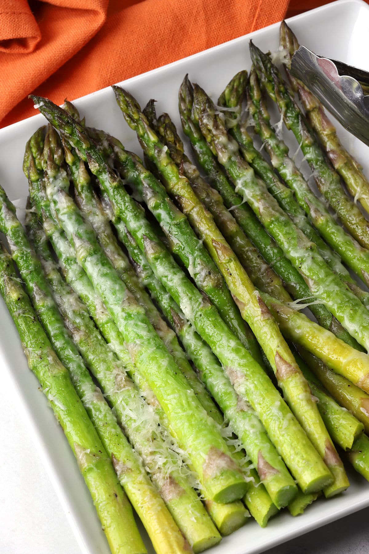 Grilled asparagus topped with melted parmesan cheese on a white serving plate.