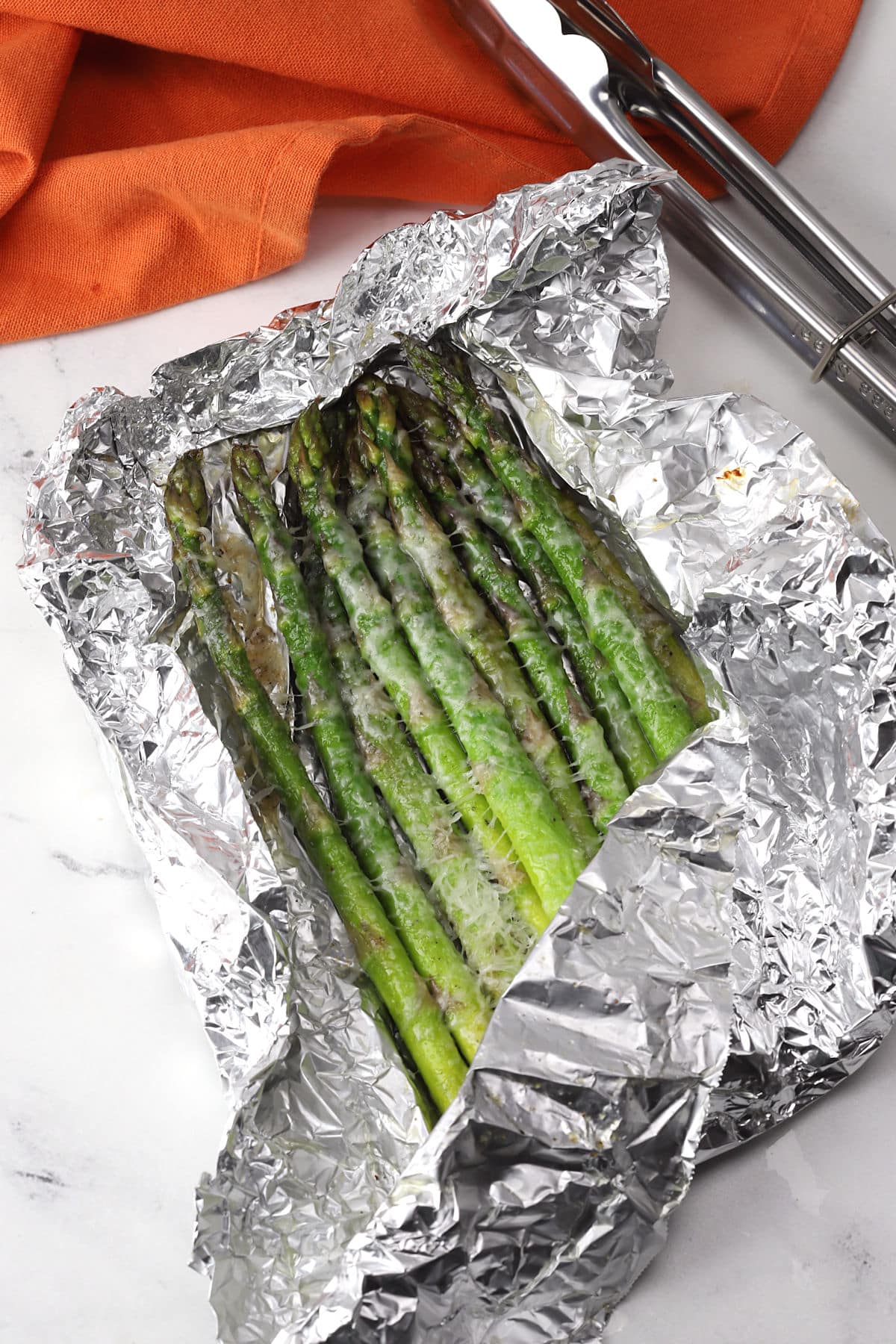 Packet of foil opened to reveal steamed asparagus topped with melted parmesan cheese.