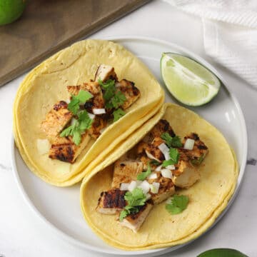 Two grilled chicken tacos in corn tortillas on a white plate.