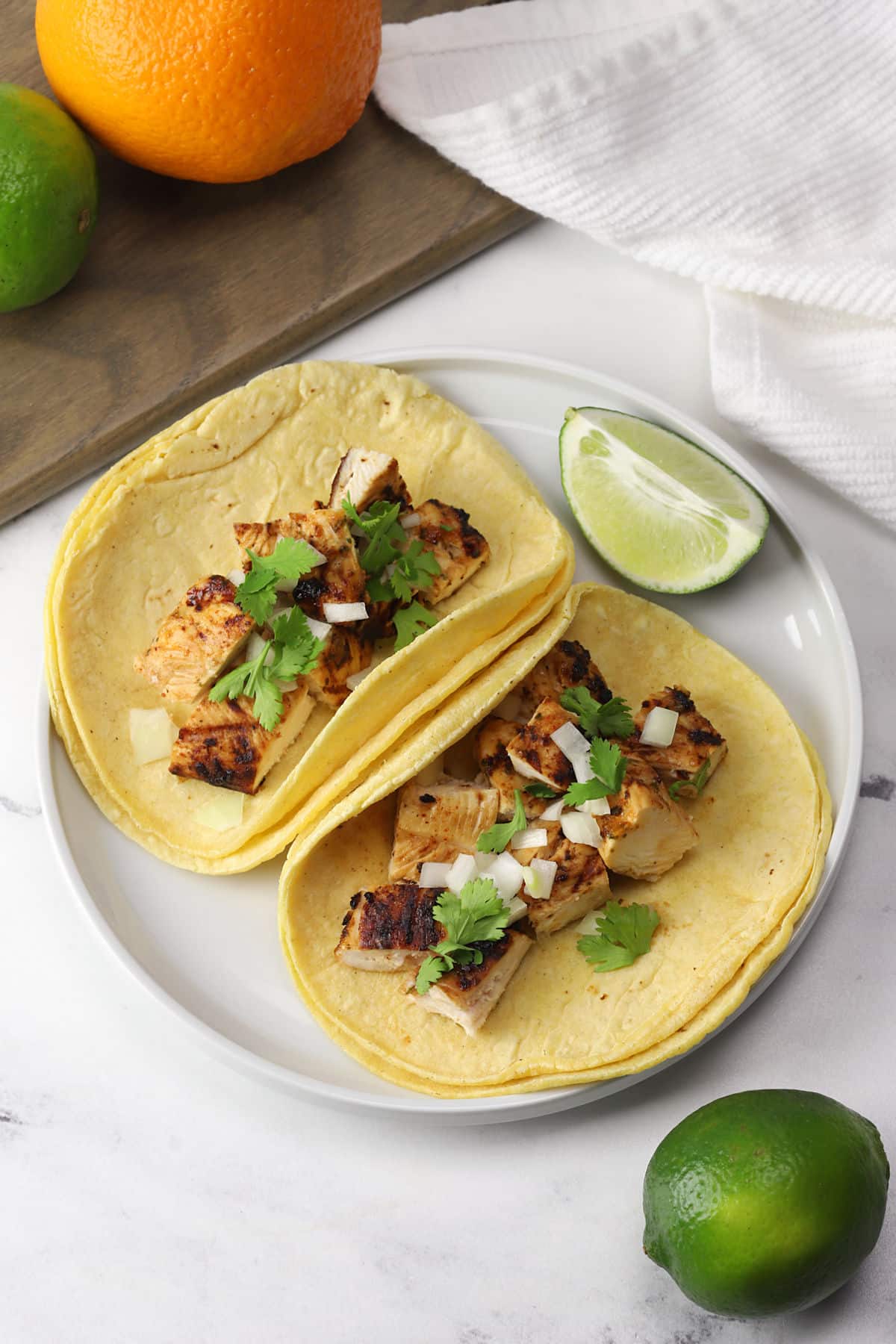 Two grilled chicken tacos in corn tortillas on a white plate.