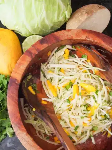 A wooden bowl of slaw with a matching wooden serving spoon.