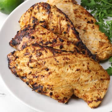Pieces of Mexican grilled chicken on a white serving plate with fresh cilantro.