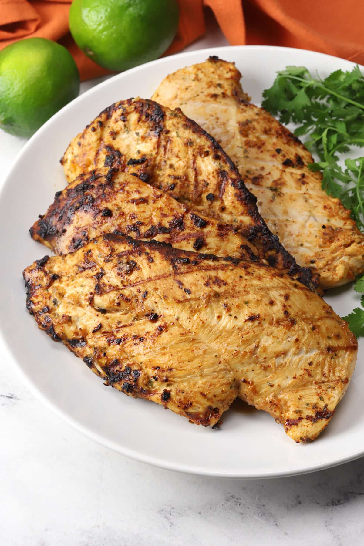 Pieces of Mexican grilled chicken on a white serving plate with fresh cilantro.
