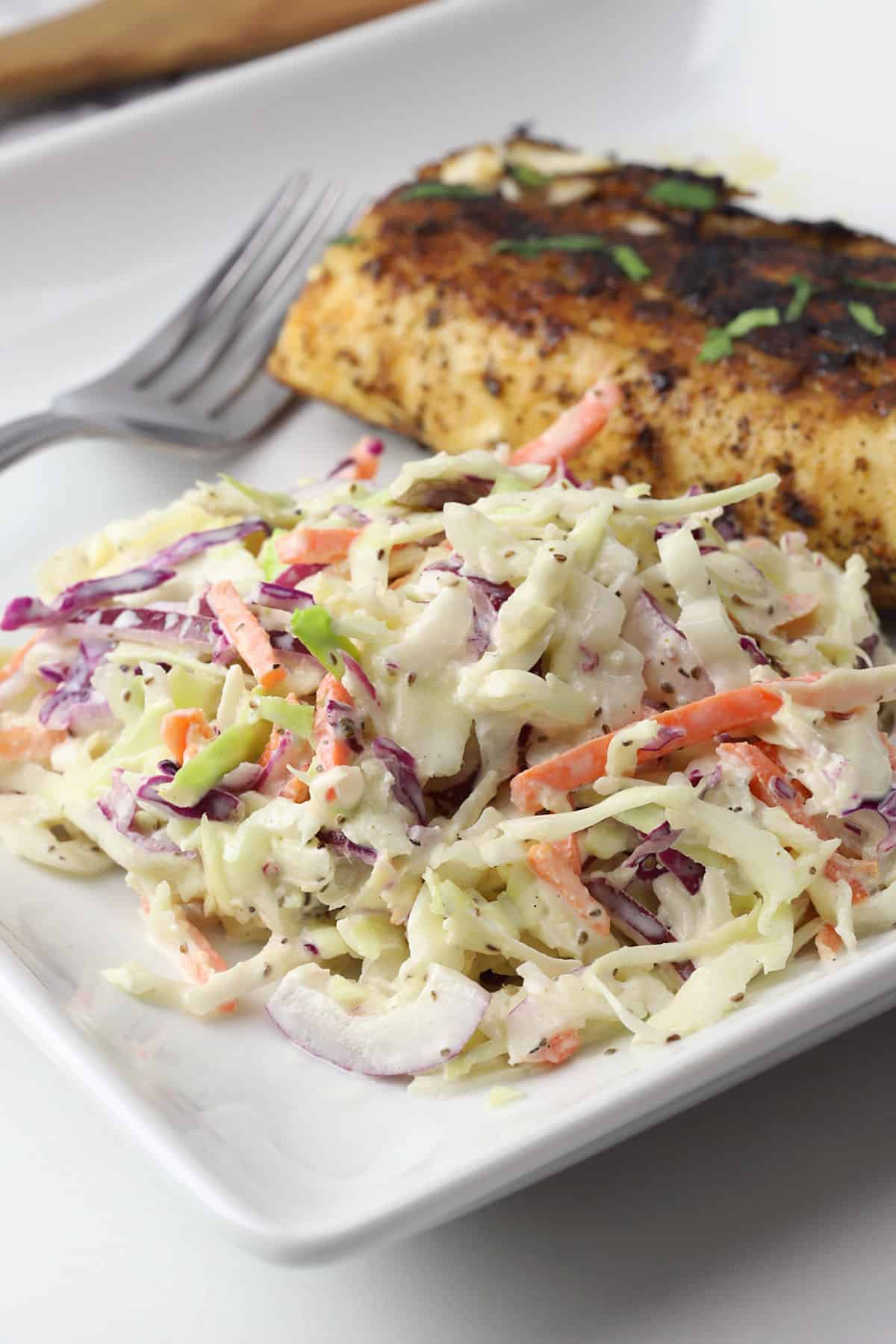 Southern coleslaw on a white plate with cooked meat and a fork in the background.