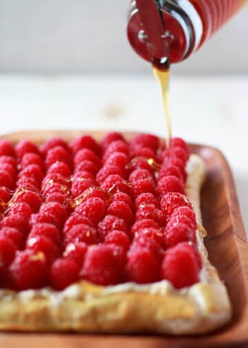 A raspberry tart being drizzled with honey.