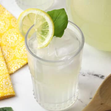 Close up of a glass of basil lemonade, garnished with a basil leaf and a lemon slice.