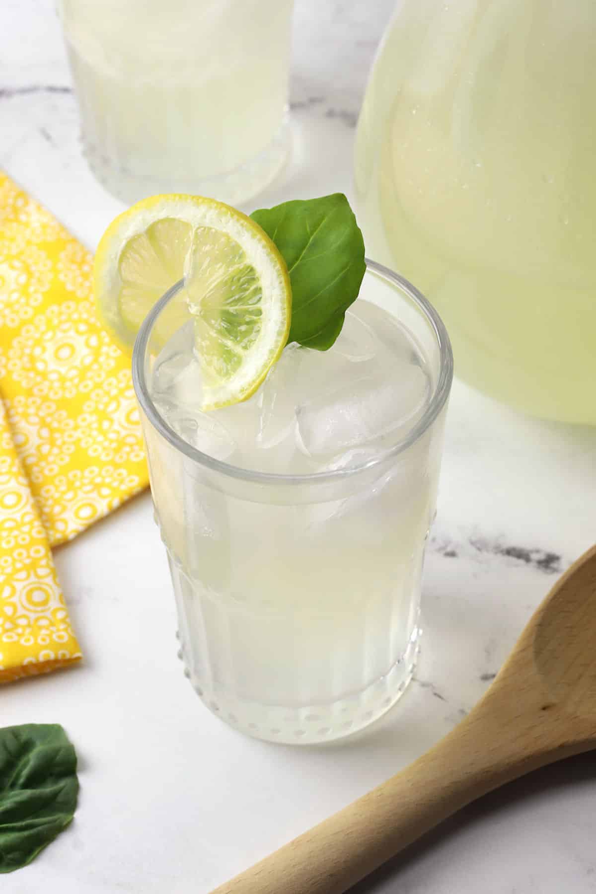 Close up of a glass of basil lemonade, garnished with a basil leaf and a lemon slice.