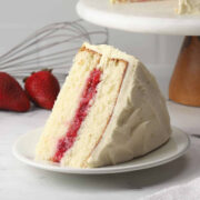 A slice of strawberry filled white cake on a white plate.