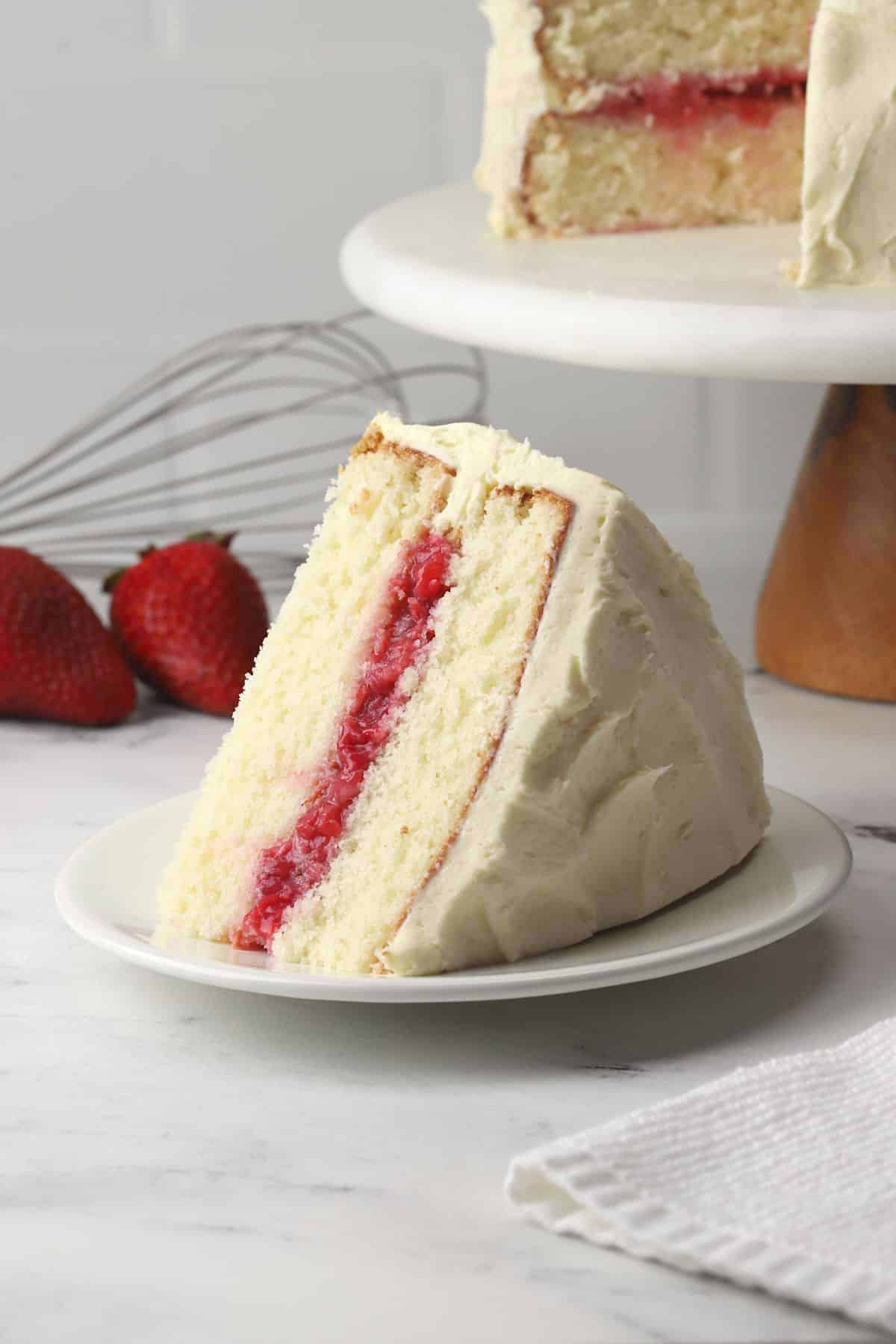 A slice of strawberry filled white cake on a white plate.