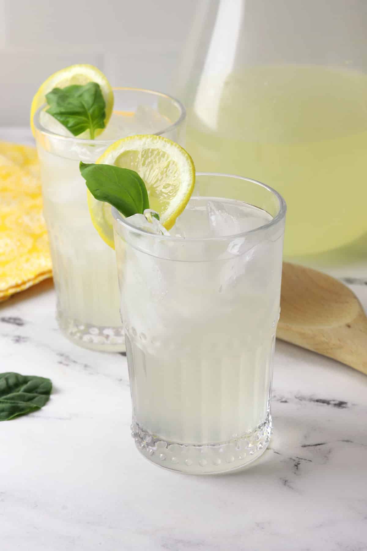 Two glasses and a pitcher filled with basil lemonade.