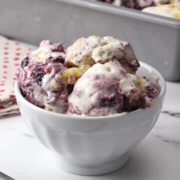 A white serving bowl filled with scoops of boysenberry ice cream.