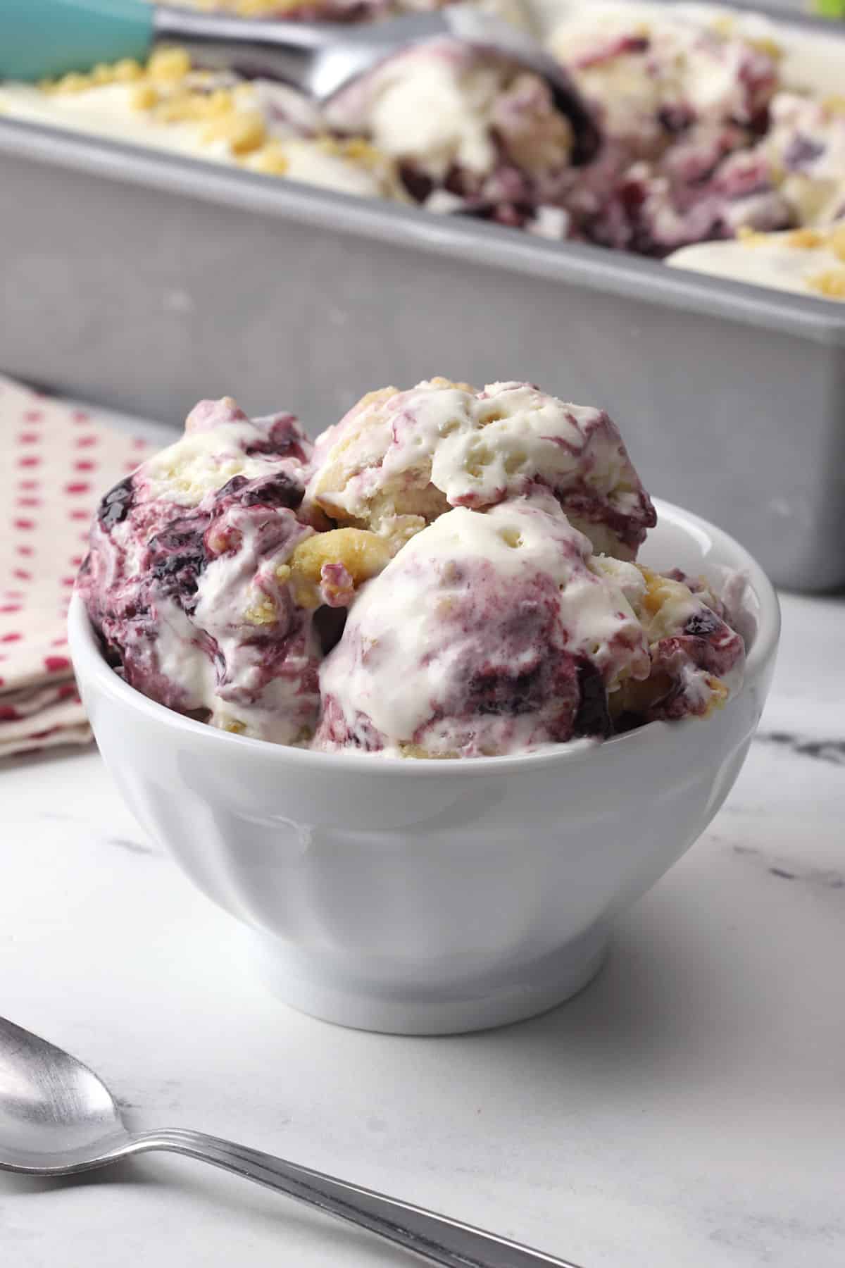 A white serving bowl filled with scoops of boysenberry ice cream.