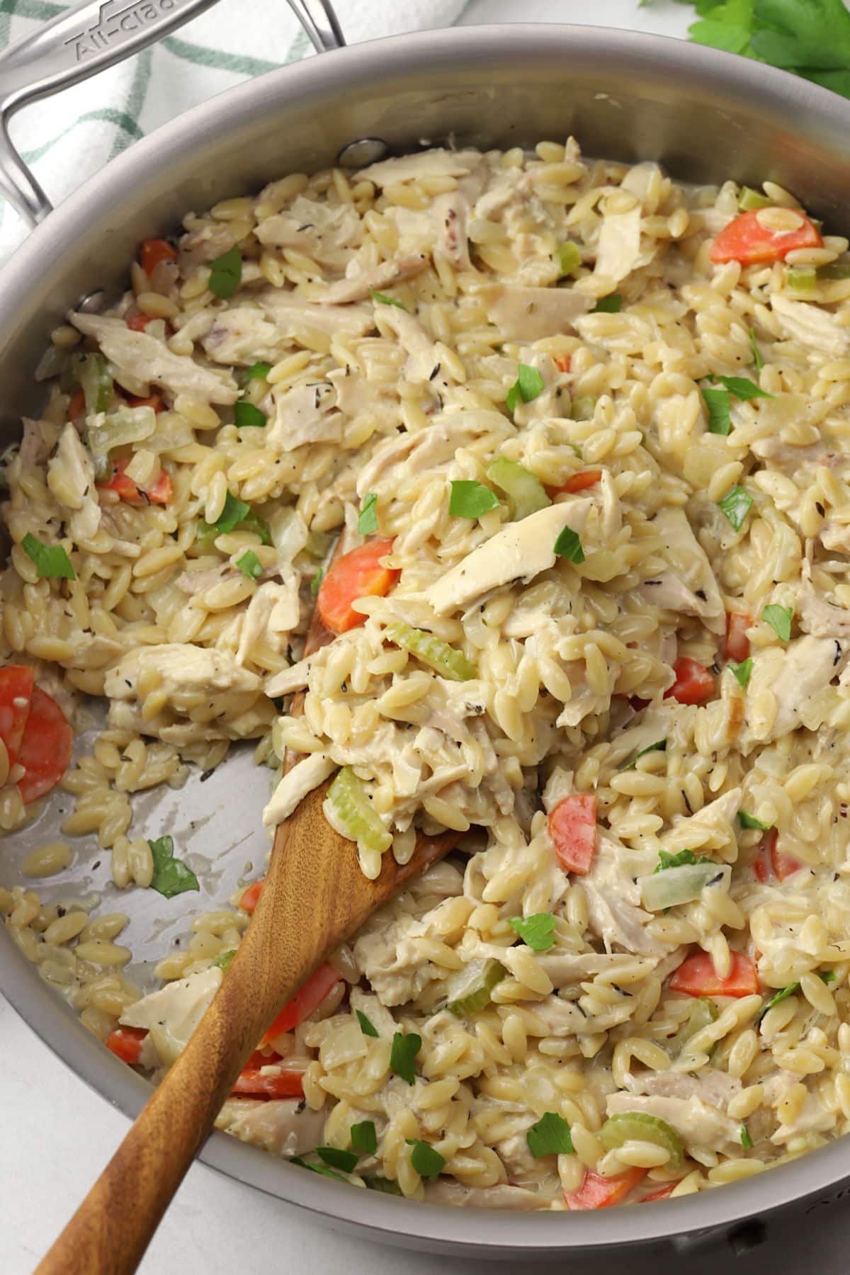 Close up of creamy chicken orzo in a skillet scooped by a wooden serving spoon.