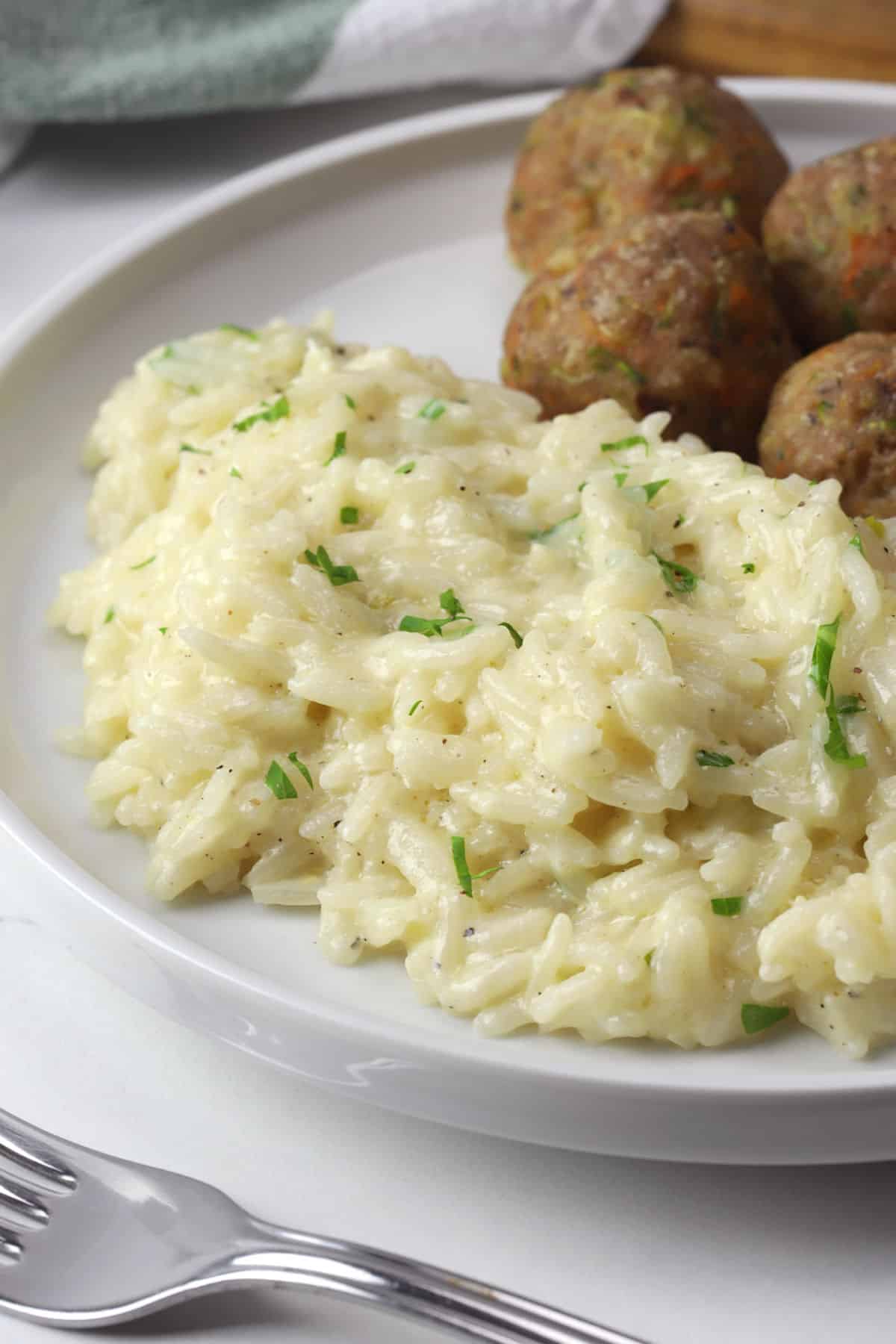 Garlic parmesan rice plated with meatballs on a white plate.