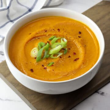 A white bowl filled with creamy pumpkin carrot soup topped with green onions.