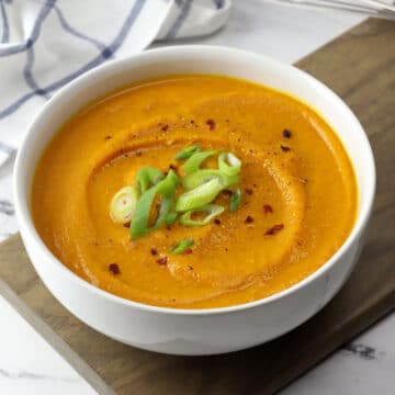 A white bowl filled with creamy pumpkin carrot soup topped with green onions.