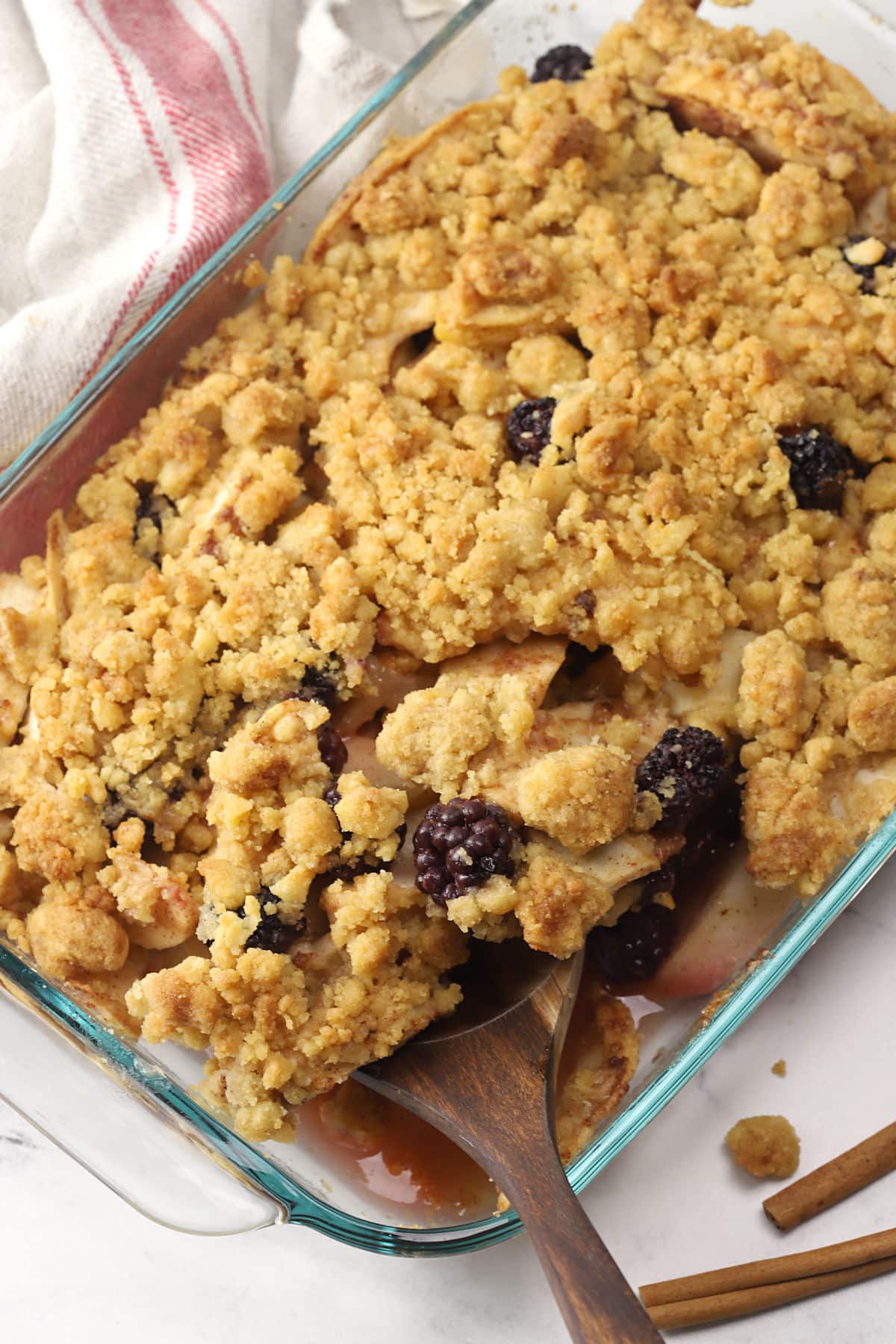 Close up of apple blackberry crumble scooped by a wooden serving spoon.