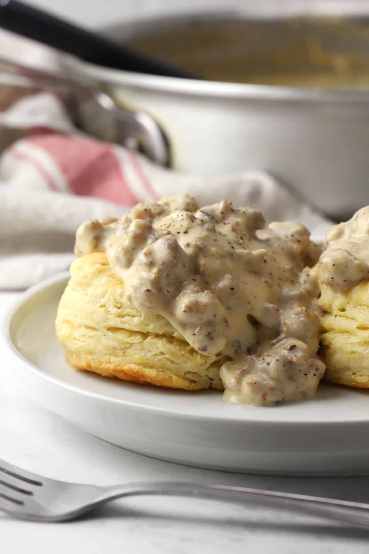 A fluffy buttermilk biscuit smothered in sausage gravy on a white plate.