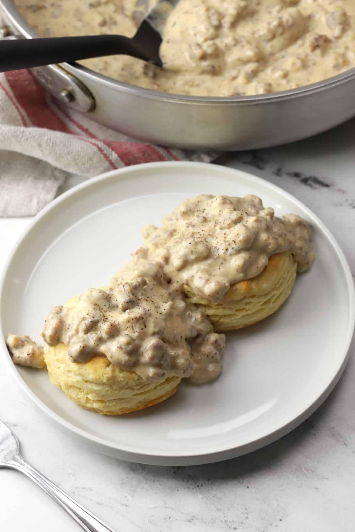 Two biscuits on a white plate topped with peppery sausage gravy.